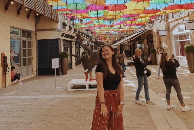 A student stands underneath The Umbrella Sky Project, an art display featuring hundreds of brightly colored umbrellas above the streets in Paris.