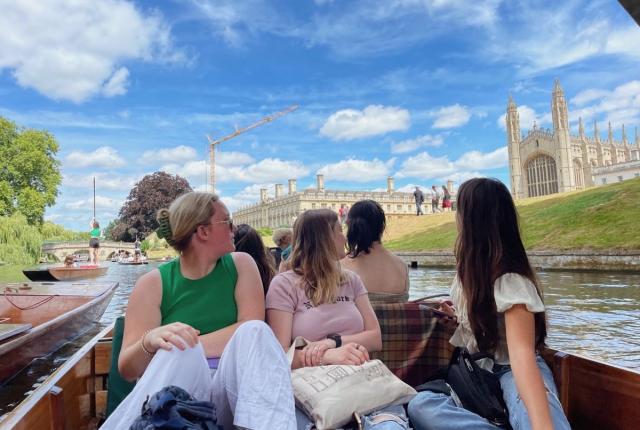 students sitting in a boat in Cambridge, looking behind them at the architecture