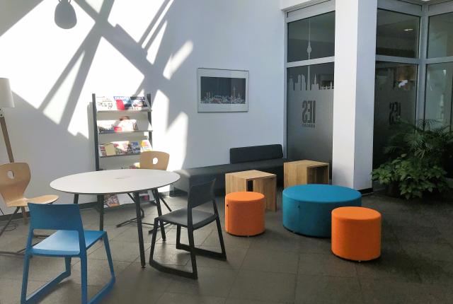 A lounge with a table and orange and blue stools.