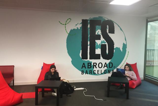 Two students sit in red lounge chairs in the Barcelona Center. Between them in a globe painted on the wall.