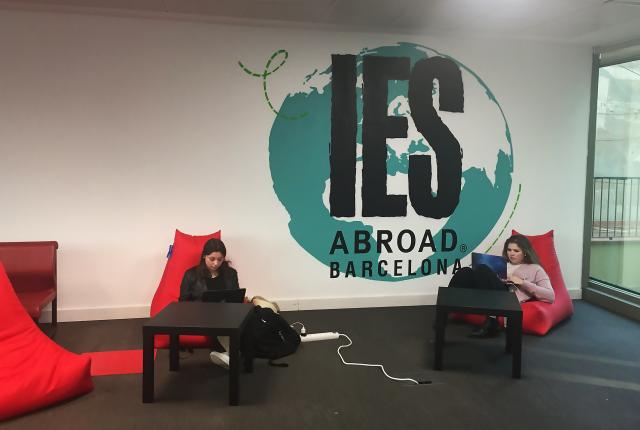 Two students sit in red lounge chairs in the Barcelona Center. Between them in a globe painted on the wall.