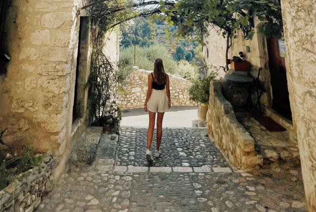 A students stands between two buildings in Nice, France. In front of her are trees.