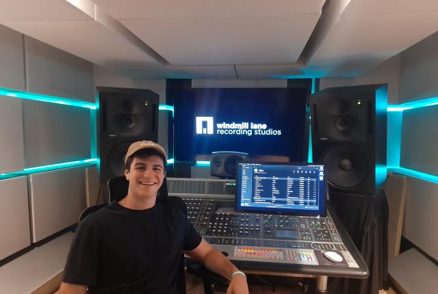 student smiling with hat on in front of audio visual equipment