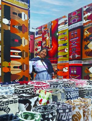 a seller at the market in Otavalo surrounded by colorful quilts