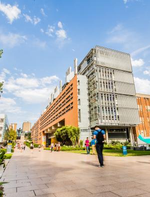 Students make their way to class on UNSW's campus, with tall brick buildings along the main walkway.