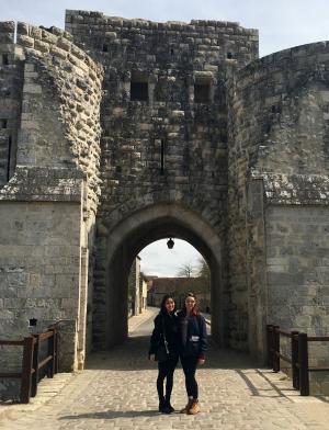 Two students stand in front of the gray stone walls of Provins. 
