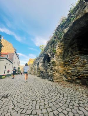 A student walks along a stone path in Maastricht on a bright day.