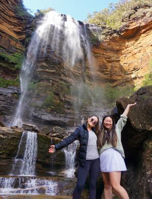 Students standing underneath a waterfall on a sunny day.