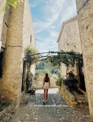 A students stands between two buildings in Nice, France. In front of her are trees.