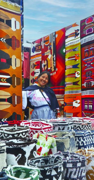 a seller at the market in Otavalo surrounded by colorful quilts