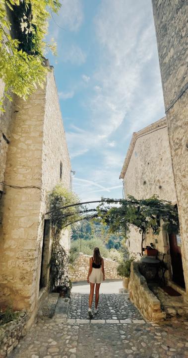 A students stands between two buildings in Nice, France. In front of her are trees.