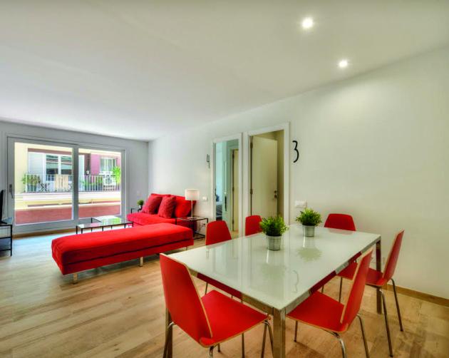 A minimalist living space featuring bright red furniture, a large window, a television, and a dining room with red chairs.