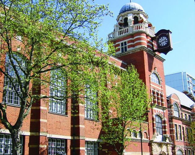 Students walk outside the University of London, a brick building with a round spire.