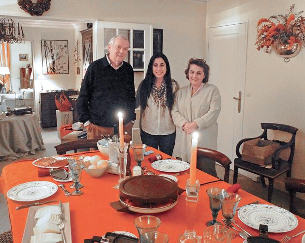 A student with their host parents standing at a set dining room table in a Paris homestay.