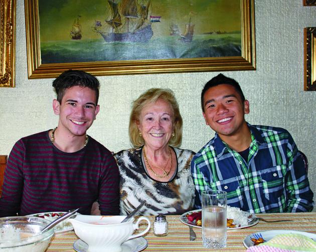 Students sit with their host mother at the dinner table, smiling at the camera.