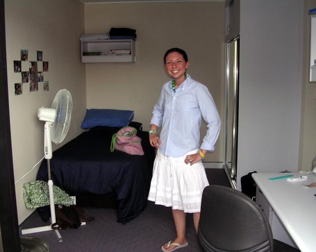 A student stands in their UNSW Shalom College student room, with a bed, a desk, and a bathroom.