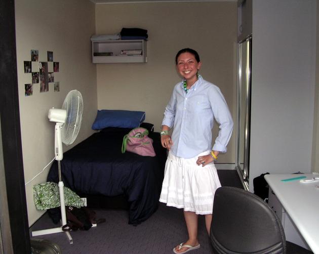 A student stands in their UNSW Shalom College student room, with a bed, a desk, and a bathroom.