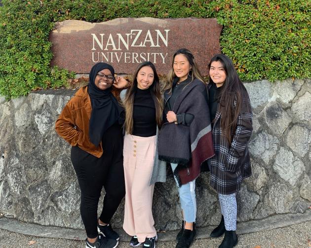 Students pose outside of Nanzan University's sign. The text reads: "Nanzan University."