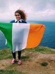 a student holding an Irish flag at the Cliffs of Moher