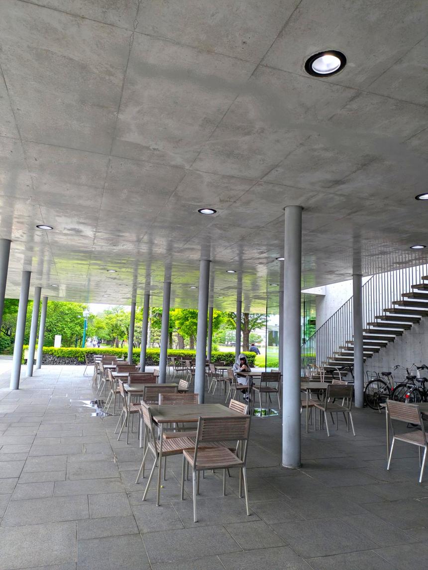 Seating area in an covered concrete patio on the Sagami Women's University campus, with a few students in the background.