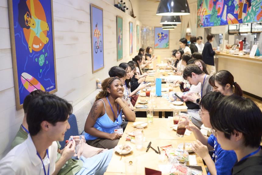 Dozens of students spread across 4 tables in restaurant, chatting and enjoying food.