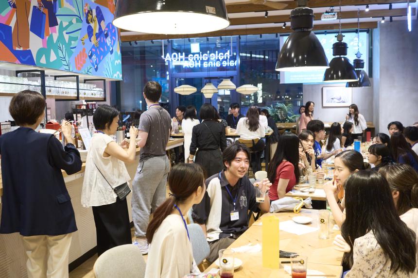 Inside the venue of the SAF Japan Alumni Party, students at tables and standing in line for food.
