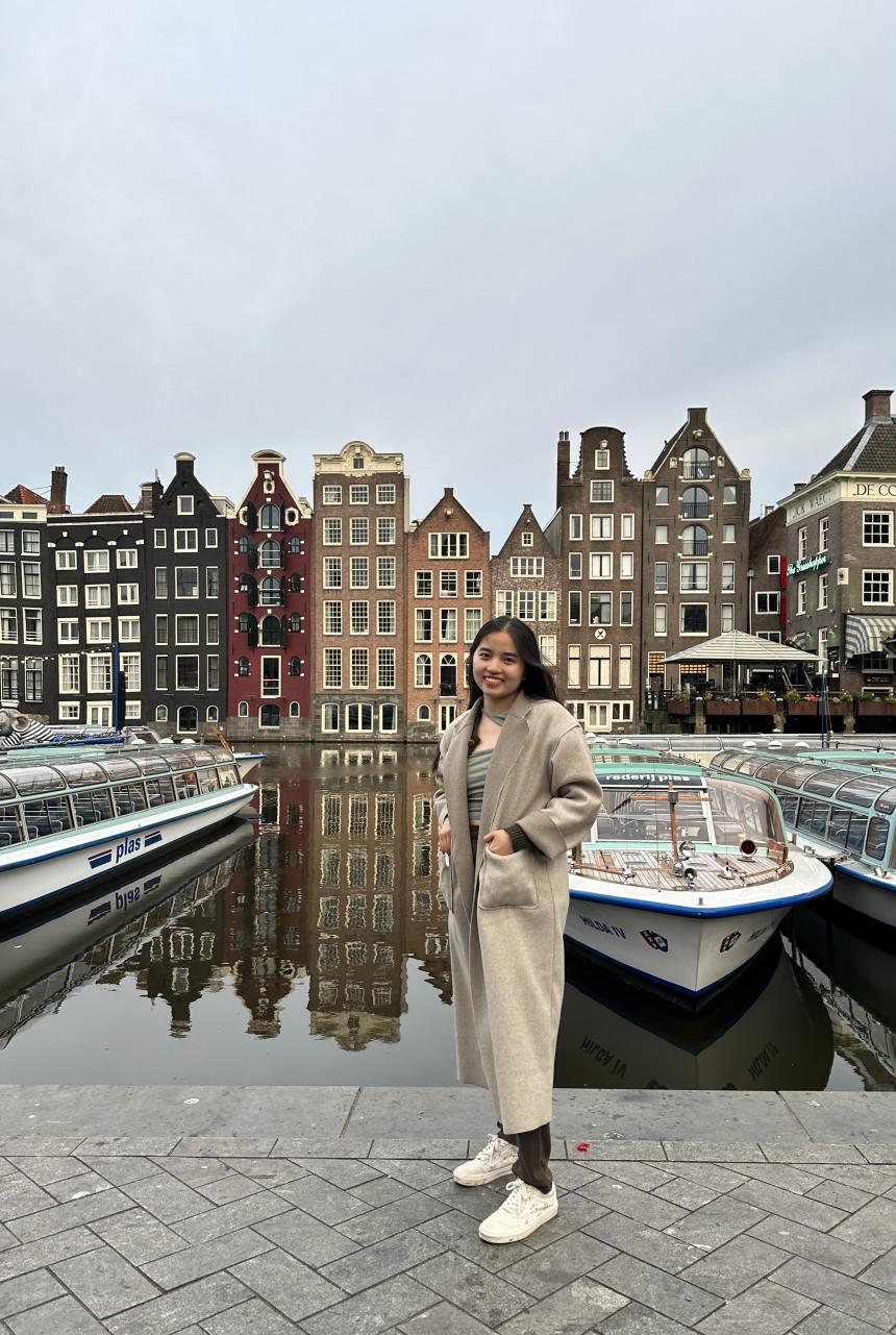Student standing in front of Boats and Rows of Houses in Amsterdam Canal