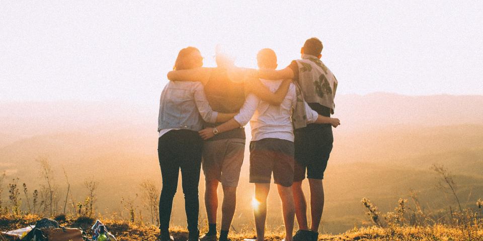 A group of friends have their arms around each other facing a sunset