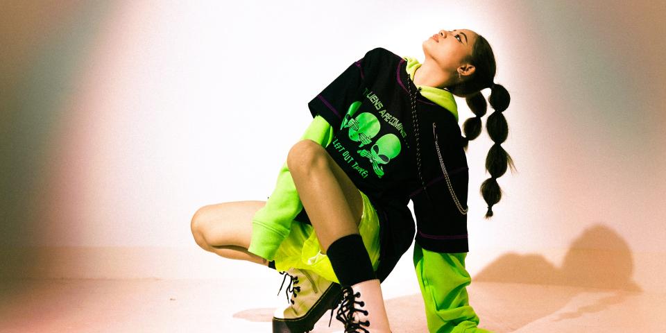 a woman in black and lime green with pink platform boots holds a pose