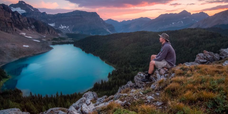 a man sits on a rock overlooking a lake at sunset